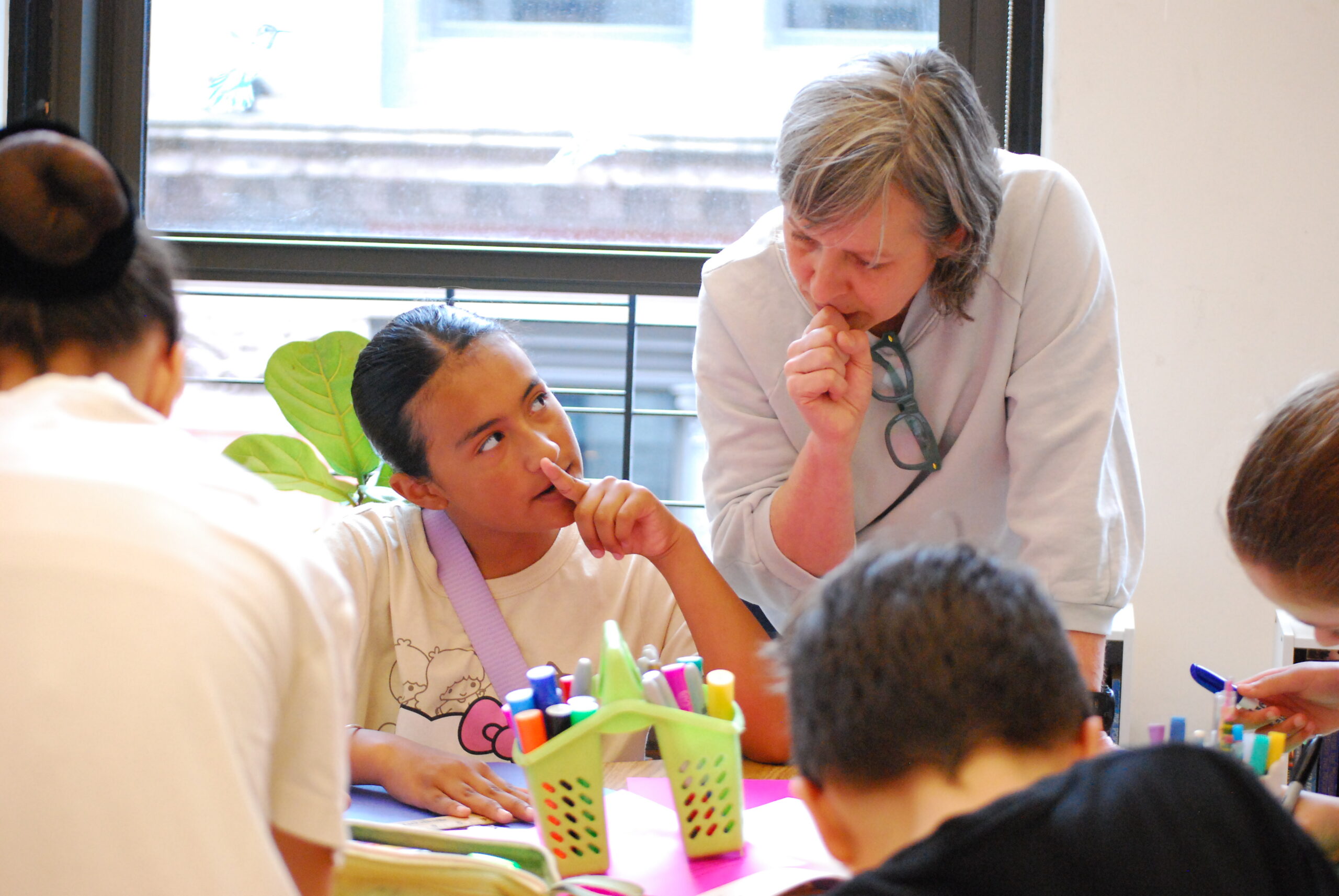 A teacher and student in a classroom look at each other, their hands held over their mouths as they appear deep in thought.