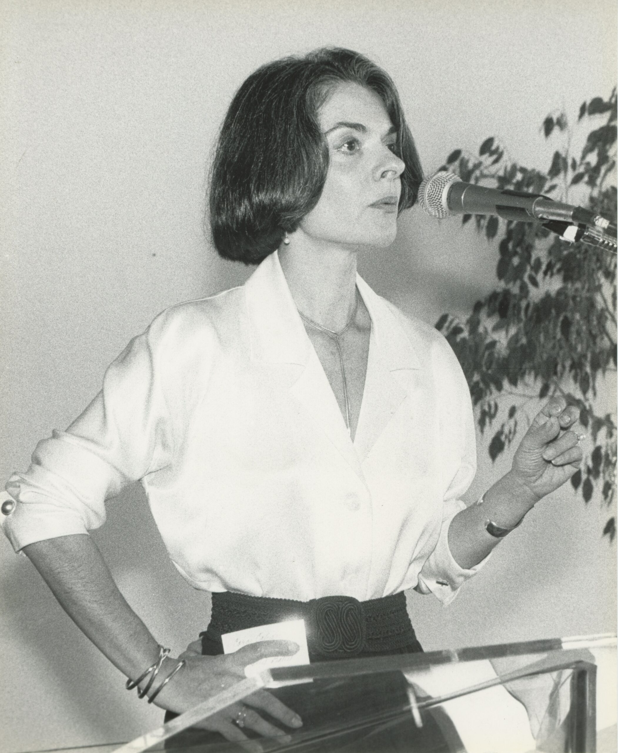 A black and white photo of Cora Cahan speaking into a microphone.