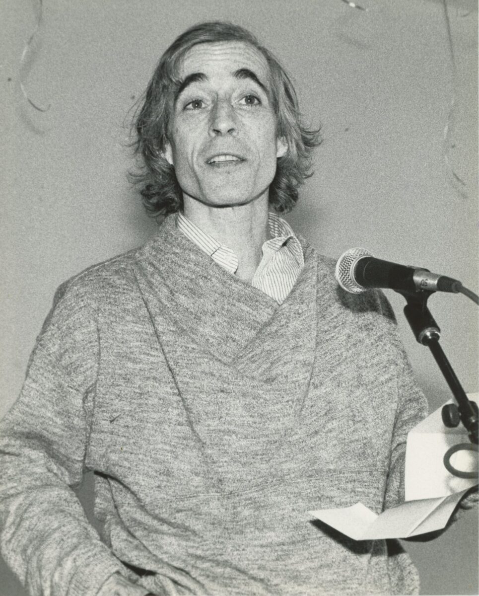 A black and white photo of Eliot Feld speaking into a microphone.
