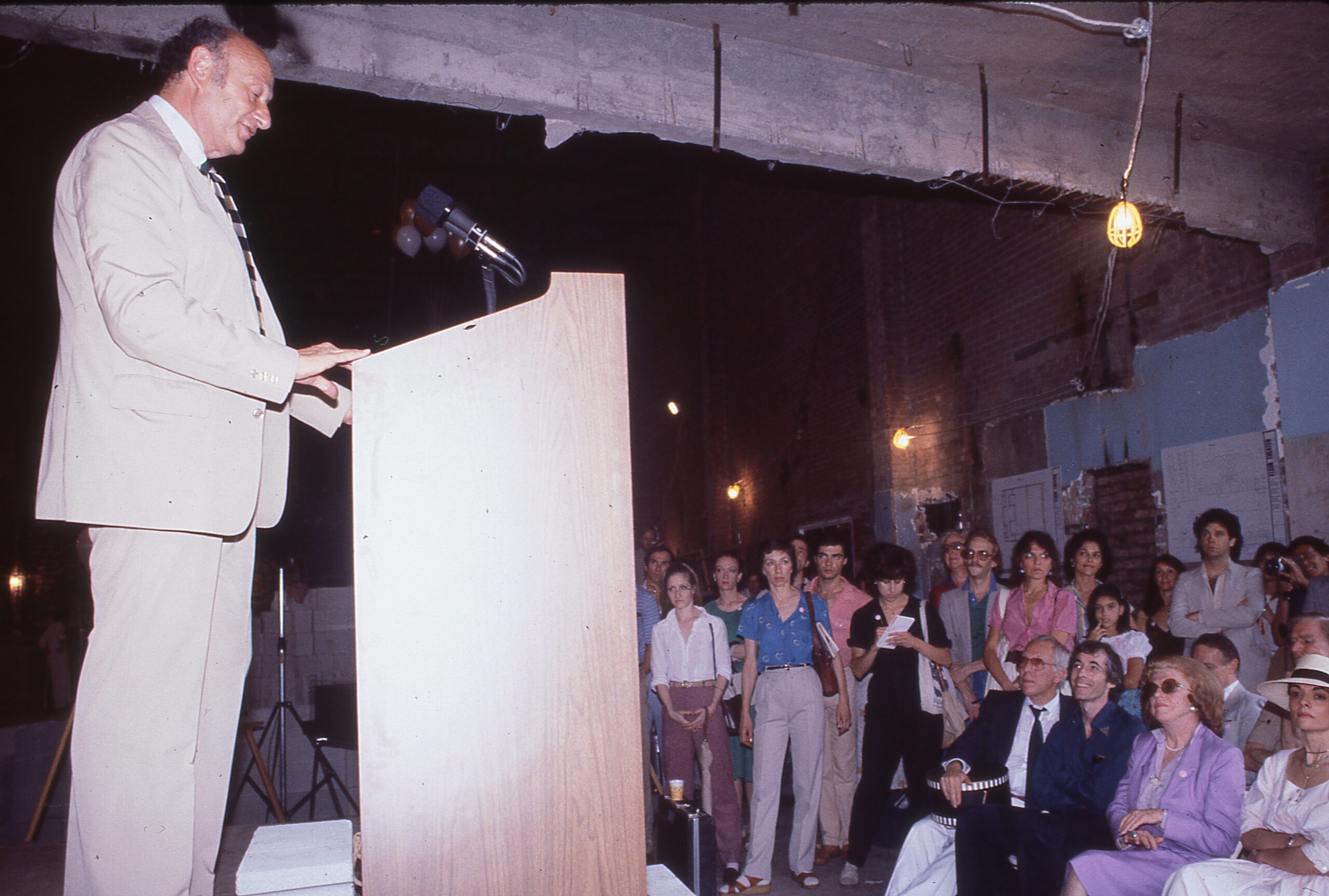 A man stands at a podium speaking to a crowd of audience members.