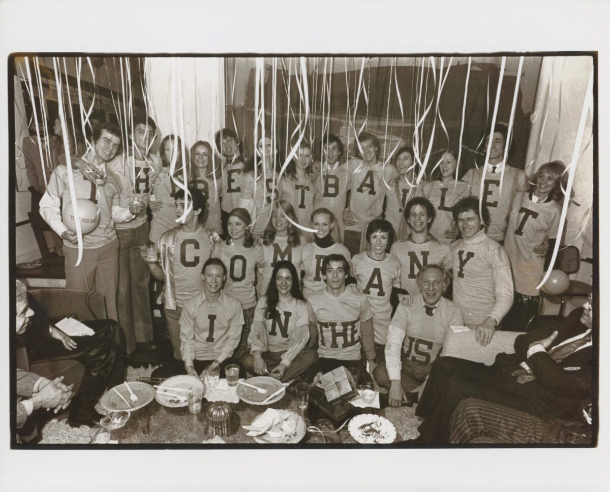 A black and white photo of Eliot Feld and his company dancers. They wear t-shirts with block lettering that spell out &quot;The Best Ballet Company in the US.&quot;