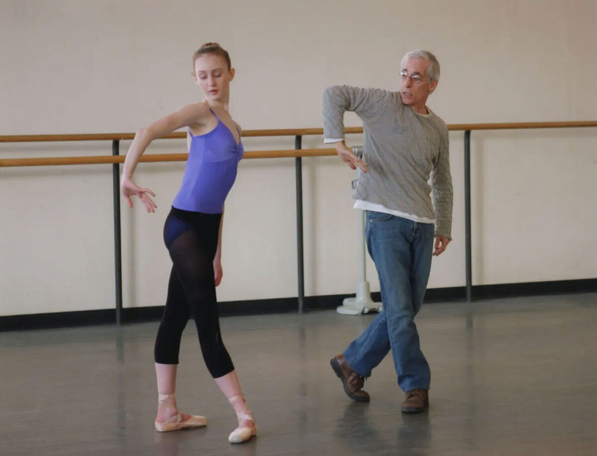 Eliot Feld rehearses in a studio with a ballet dancer. She copies the curved, inverted shape he is making with his elbow and wrist.