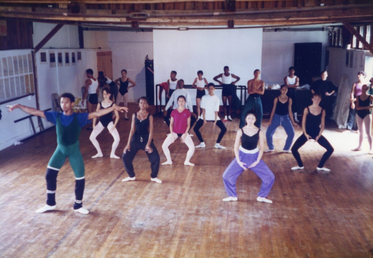 Students in dancewear and warmups practice plies in the center in a dance studio at Jacobs Pillow.