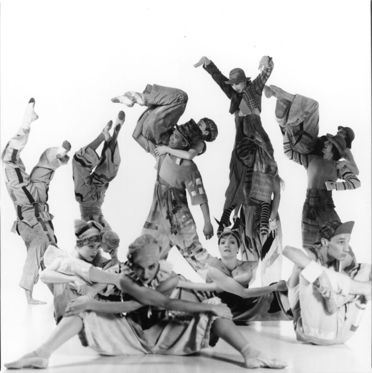 Black and white photo of Eliot Feld&#039;s &quot;Paper Tiger.&quot; The dancers wear clownish costumes. They hug their legs to their torsos, do handstands, and pick each other up.