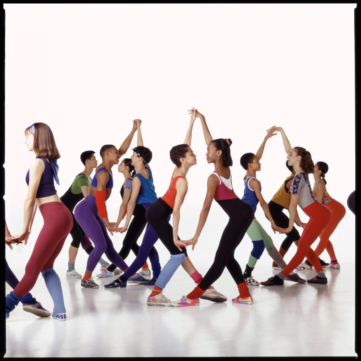 Students in colorful leotards and leggings perform Eliot Feld&#039;s &quot;The Jig Is Up.&quot; They are coupled up in partners, dancing together while holding hands.